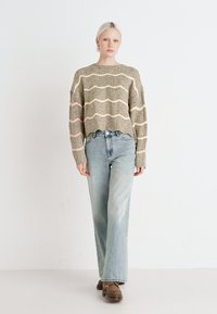 Suéter de punto en verde oliva con rayas onduladas en beig y rosa, combinado con unos vaqueros de pierna ancha en azul claro y zapatos marrones.