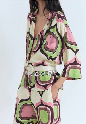 Multikleurige blouse- en broekset met een gedurfd geometrisch patroon in roze, groen en bruin, een losse pasvorm en brede mouwen, geaccentueerd met een witte riem.