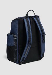 Marinblå rygsæk med netbag, justerbare stropper, frontlomme med lynlås og en belagt bund. Har brandingdetaljer og et struktureret design.