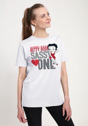 Hvid bomulds t-shirt med et grafisk print af Betty Boop i en rød kjole, med sort og rød tekst der siger "BETTY BOOP SASSY ONE" og hjerte-design.
