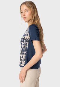 Top de manga corta azul marino con un frente texturizado de patrón en crema y azul marino. Tela suave, diseño ajustado y detalle de dobladillo acanalado.