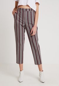 Kvinna iförd högmidjade kapade byxor med vertikala svart- och röd-ränder och geometriska mönster, i kombination med vita ankelskor och en kapad vit topp.