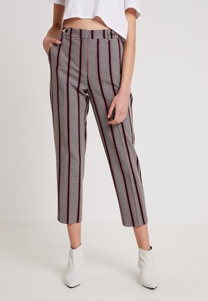 Kvinna iförd högmidjade kapade byxor med vertikala svart- och röd-ränder och geometriska mönster, i kombination med vita ankelskor och en kapad vit topp.