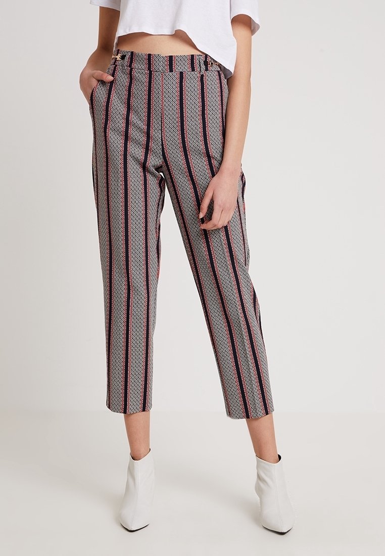 Kvinna iförd högmidjade kapade byxor med vertikala svart- och röd-ränder och geometriska mönster, i kombination med vita ankelskor och en kapad vit topp.