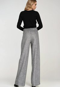 Spodnie o szerokich nogawkach w szarym wzorze w pied de poule, z elastycznym czarnym pasem. Gładka tekstura i długość do pełnych nóg. Czarny top z długim rękawem.