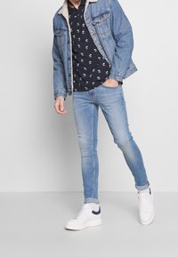 Jeansjacka med pälskrage, mönstrad marinblå skjorta, ljusblå tajta jeans och vita sneakers med marinblå detaljer.