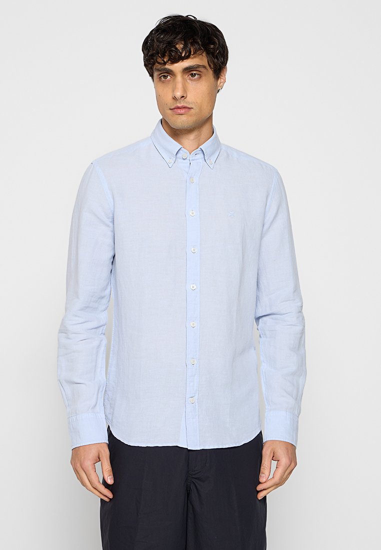Chemise bleu clair à manches longues avec boutons, fabriquée à partir d'un tissu texturé, présentant un col classique et des boutons blancs sur le devant.