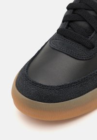Baskets noires en cuir lisse et suède texturé. Semelle en caoutchouc arrondie avec une finition translucide couleur gomme.