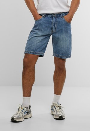 Hellblaue Denim-Shorts mit einer regulären Passform, Fünf-Taschen-Design und dezentem Verblassen. Kombiniert mit grauen und blauen Sportschuhen.
