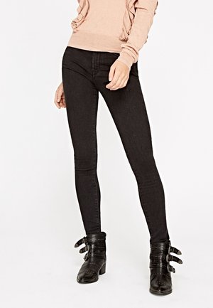 Jeans skinny negros con una textura de denim suave, combinados con botas negras hasta el tobillo que tienen múltiples hebillas y acentos de tachuelas.