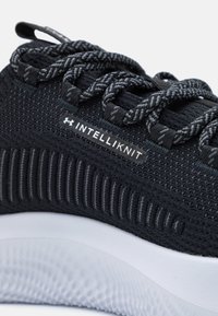 Sort sportsko med en tekstureret strikoverdel, mønstrede snørebånd og en hvid sål med en honningkage-struktur. Logo synligt på siden.