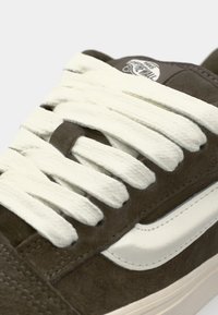 Brown suede skate shoe with white laces. Features a white leather stripe and textured surface on the upper. Close-up of the lace area.