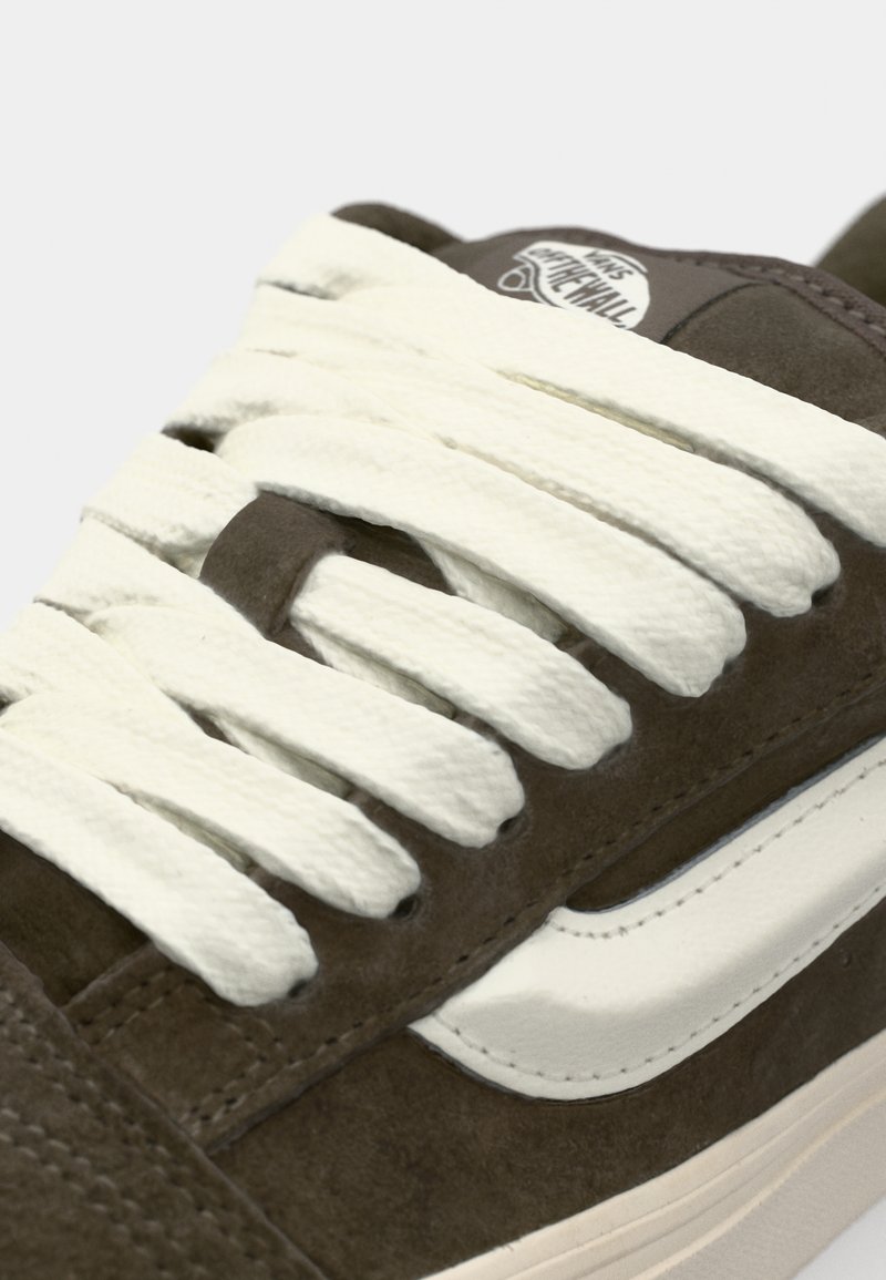 Braunes Wildleder-Skate-Schuh mit weißen Schnürsenkeln. Verfügt über einen weißen Lederstreifen und eine strukturierte Oberfläche im oberen Bereich. Nahaufnahme des Schnürbereichs.