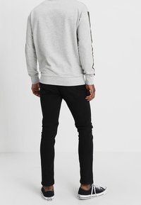 Sudadera gris de mangas largas, con puños y dobladillo de canalé. Combinada con jeans negros ajustados y zapatillas negras con suelas blancas.