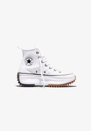Białe, wysokie trampki Converse z grubą, dwukolorową, postrzępioną podeszwą, metalowymi oczkami i naszywką z logo „Chuck Taylor All Star” po boku.