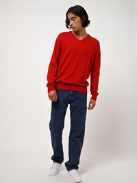 Maglione rosso a maglia con scollo a V, vestibilità ampia, indossato con jeans a gamba dritta blu scuro e sneakers bianche. Tessuto liscio, design casual.