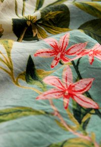 Close-up of fabric featuring vibrant pink flowers and green leaves against a light blue background, showcasing intricate floral patterns.