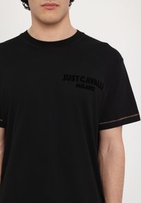 Svart bomull T-skjorte med rund hals, pyntet med en subtil fløyelslogo "JUST CAVALLI MILANO" på brystet og oransje sømmer på ermene.
