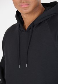 Svart huvtröja med snörning, tillverkad av mjukt, strukturerat tyg och med en avslappnad passform. Detaljer inkluderar snören med silverändar.