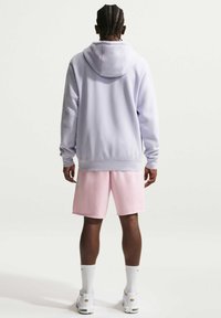 Vaaleanpunainen huppari, jossa säädettävä huppu ja resorit hihansuissa, yhdistetty vaaleanpunaisiin shortseihin. Kangas vaikuttaa pehmeältä; väljä istuvuus, yksinkertainen muotoilu.