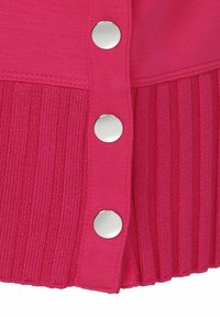 Vêtement en tricot fuchsia avec une texture côtelée, des panneaux lisses et des boutons pression en métal argenté sur le côté.