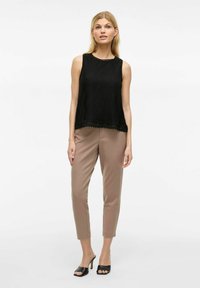 Must mõõdmatu must top tekstureeritud kudumisega ja lainelise äärisega, koos heledate pruunide kitsaste pükstega ja mustade avatud varvastega plokk-kontsaga kingadega.