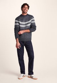 Gray knitted sweater featuring a white zigzag pattern, paired with dark jeans and white sneakers. Textured fabric and ribbed cuffs.