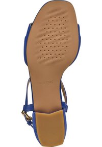 Sandale en daim bleu avec une semelle en caoutchouc brun lisse présentant un motif texturé et une boucle dorée sur la sangle de la cheville.