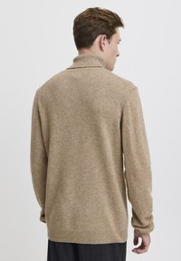 Maglione beige lavorato a maglia con collo alto e maniche lunghe. Tessuto morbido, vestibilità ampia e colore uniforme senza motivi o dettagli.