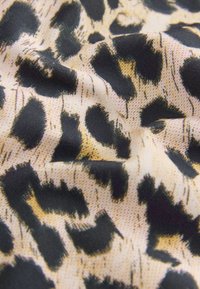 Tissu imprimé léopard avec de grandes taches noires sur un fond beige, présentant une texture lisse et un léger éclat.