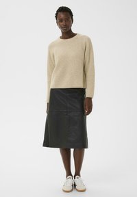 Pull en tricot beige à coupe décontractée, associé à une jupe midi en cuir noir et à des baskets blanches. Texture lisse et design simple.