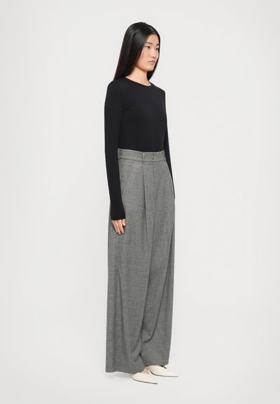 Haut noir à manches longues associé à un pantalon gris à carreaux taille haute et jambes larges, avec des ballerines blanches à bout pointu. Coupe simple, moderne et fit décontracté.
