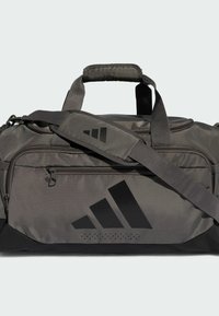 Bolsa de viaje de tela gris oscuro con un logo negro. Cuenta con asas dobles, una correa de hombro ajustable y compartimentos con cremallera.