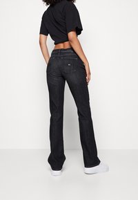 Jeans en denim noir évasés à taille haute, avec deux poches arrière et des coutures visibles, complétés par un haut noir court.