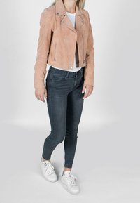 Ljusrosa mocka kort bikerjacka med silverdragkedjor, kombinerad med mörkgrå skinny jeans och vita sneakers.