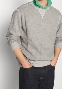 Gray sweatshirt with long sleeves, ribbed cuffs, and a crew neckline, layered over a green collared shirt. Textured fabric, casual fit.