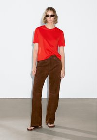 T-shirt rossa in cotone abbinata a pantaloni svasati in suede marrone, sandali e occhiali da sole. Design semplice con vestibilità comoda e texture morbida.