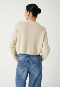 Gehaakte crèmekleurige trui met een cropped ontwerp, met textuur kabelbreisels aan de mouwen; gecombineerd met hoge taille blauwe spijkerbroek.