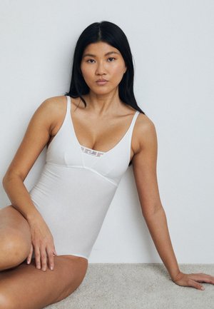 Valkoinen body, jossa on säädettävät olkaimet, muotoiltu design ja teksturoitu sisäänleikkaus kaula-aukossa. Sujuva kangas neutraalilla taustalla.