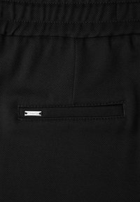 Pantalones negros de tela texturizada, con cintura elástica y un bolsillo trasero con una pequeña etiqueta metálica.