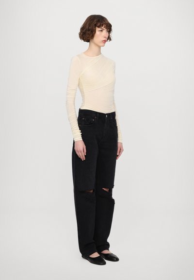 Light yellow long-sleeve top with gathered texture, paired with high-waisted black distressed wide-leg jeans and black flats.