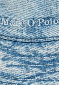 Jasnoniebieska tkanina dżinsowa z przeszytymi liniami; haftowany logo "Marc O'Polo" w białym kolorze, wyraźnie widoczne.