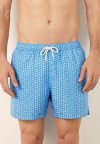 Pantaloni da bagno blu con motivo a stelle bianche, vita elastica con coulisse e tessuto leggero dalla texture morbida.