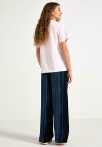 Lys lyserød bomulds T-shirt med korte ærmer, parret med mørkeblå vertikale stribede brede bukser i fløjl og farverige sko.