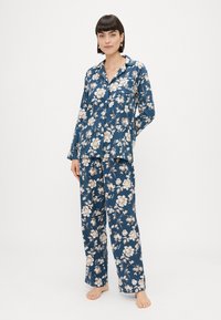 Pajama set s cvetnim vzorcem v temno modri barvi, ki vključuje dolge rokave in široke hlače, izdelan iz mehkega materiala z gumbnim detajlom.