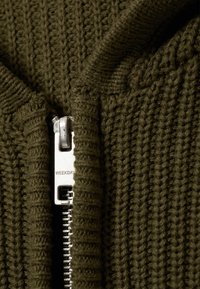 Olivazöld kötött zipzáras pulóver bordázott mintával, ezüst színű cipzárral, amelyen a "WEEKDAY" felirat található a húzón.