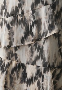 Tissu superposé avec une texture douce et plissée en imprimés léopard beige et noir, avec de subtils accents de volants le long des bords.