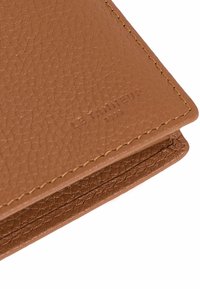 Portefeuille en cuir marron texturé avec des coutures visibles, doté d'un détail de logo en relief. Forme compacte avec des bords lisses et un motif de grain subtil.