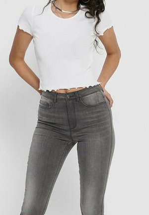 Top blanco de manga corta con bordes deshilachados, combinado con jeans ajustados gris desgastado de cintura alta que cuentan con cinco bolsillos y detalles sutiles.