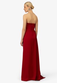 Trägerloses rotes Kleid mit taillierter Oberseite und fließendem Rock. Glattes Material mit verdecktem Reißverschluss im Rücken. Bodenlanges Design.